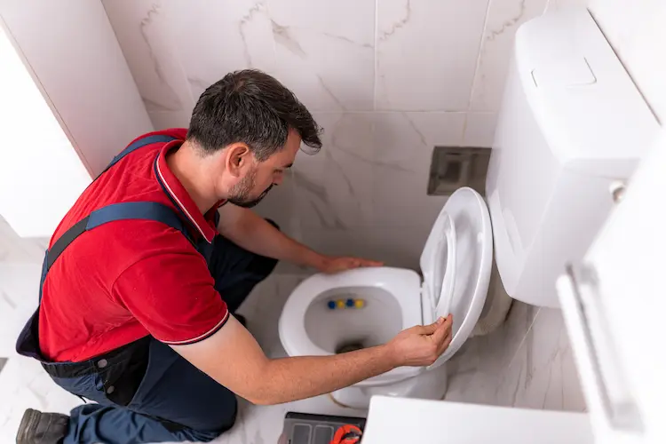 Idraulico che sistema un wc in un bagno piastrellato